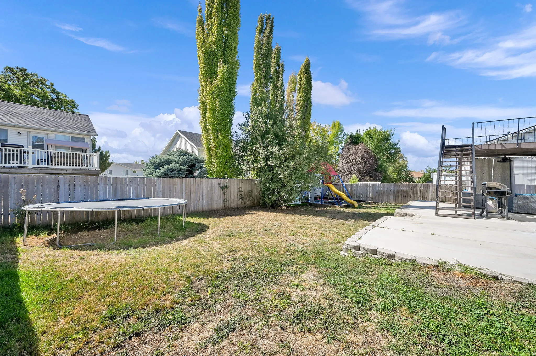 Spacious backyard featuring a concrete patio, wood privacy fencing, and mature vertical trees