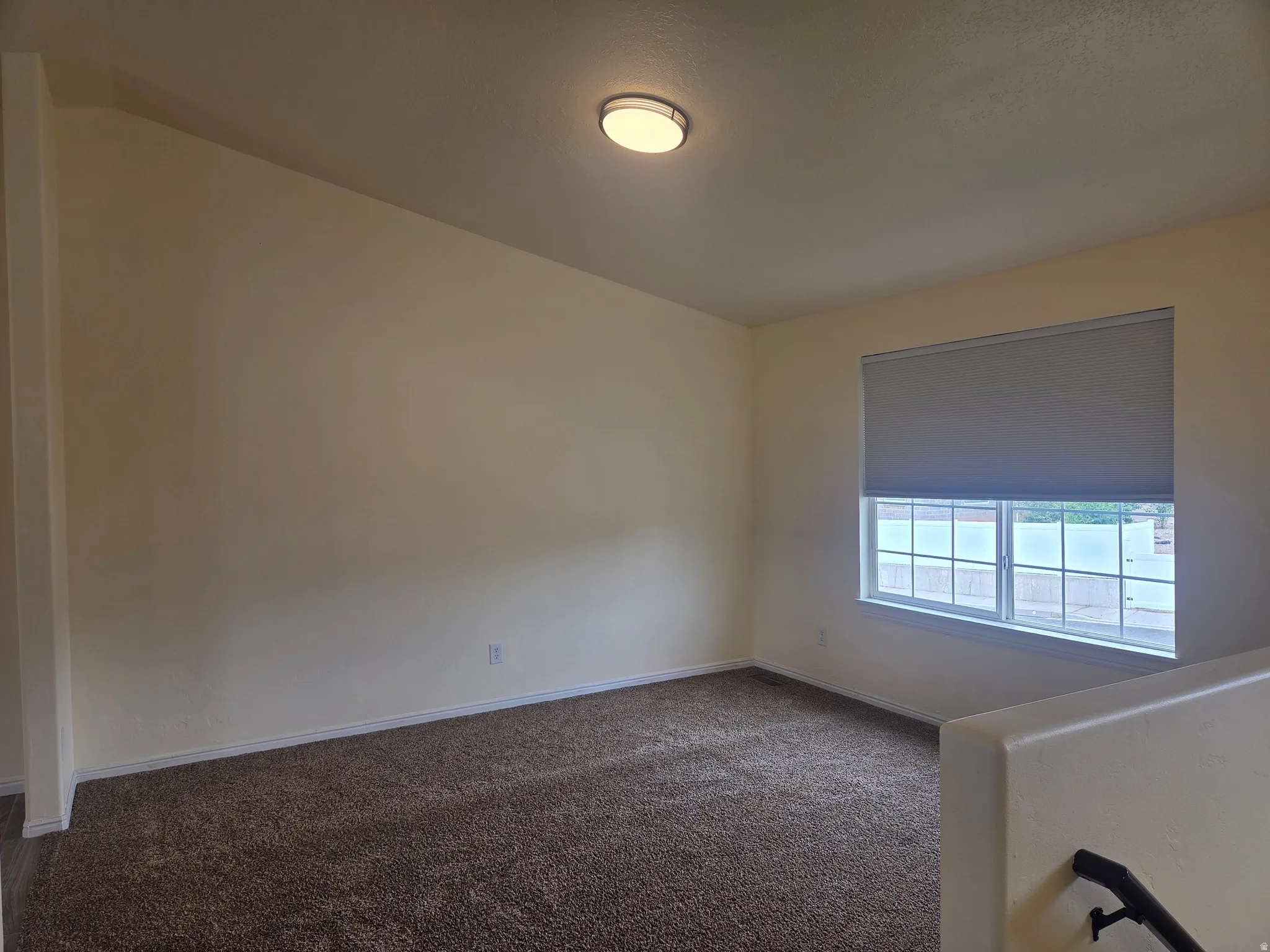 Carpeted interior space featuring light-toned walls, a flush-mount ceiling light, and a window with blinds