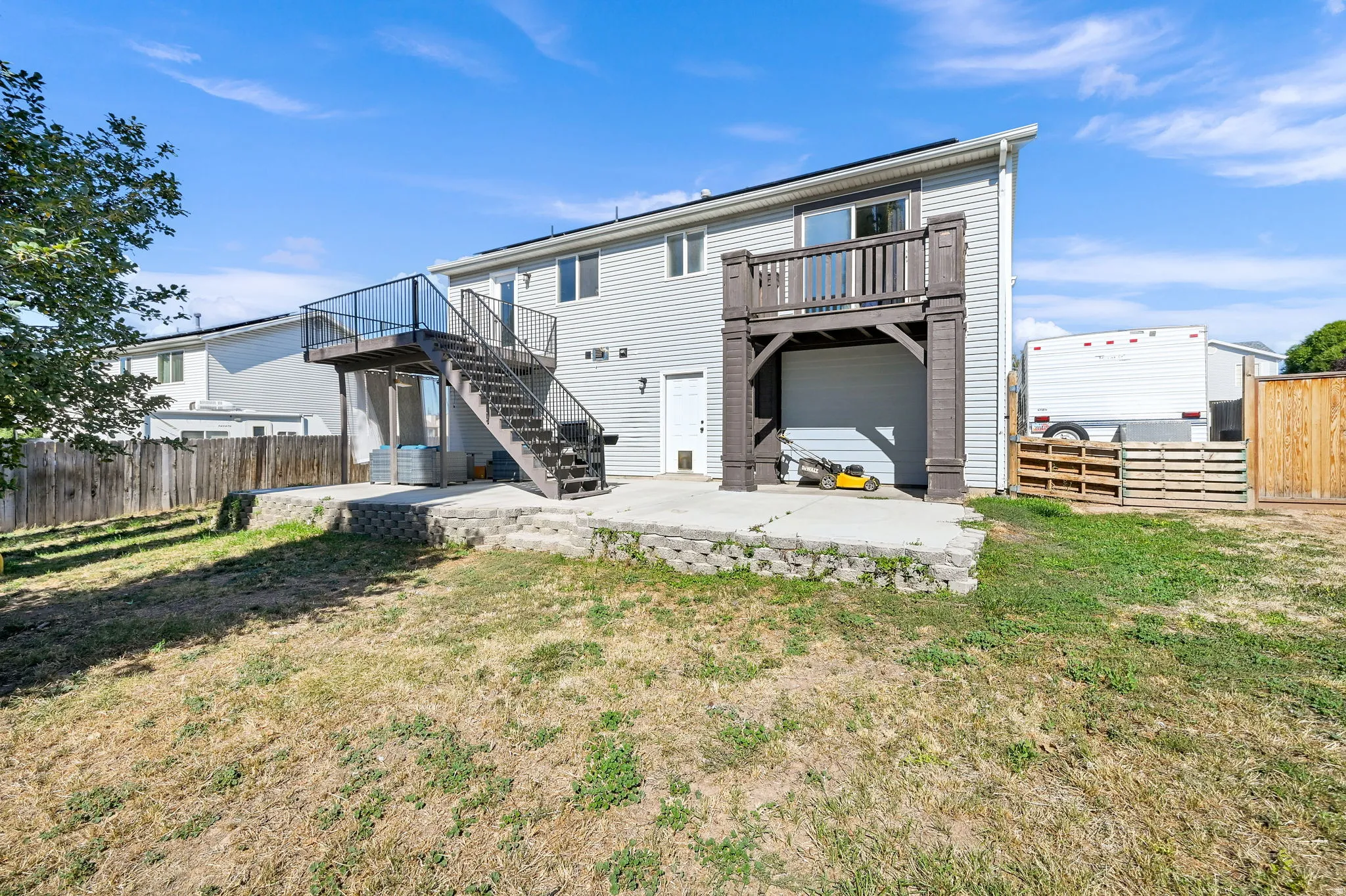 Two-story property featuring light gray siding, a concrete patio, a wooden fence, and a multi-level deck with black railings and stairs