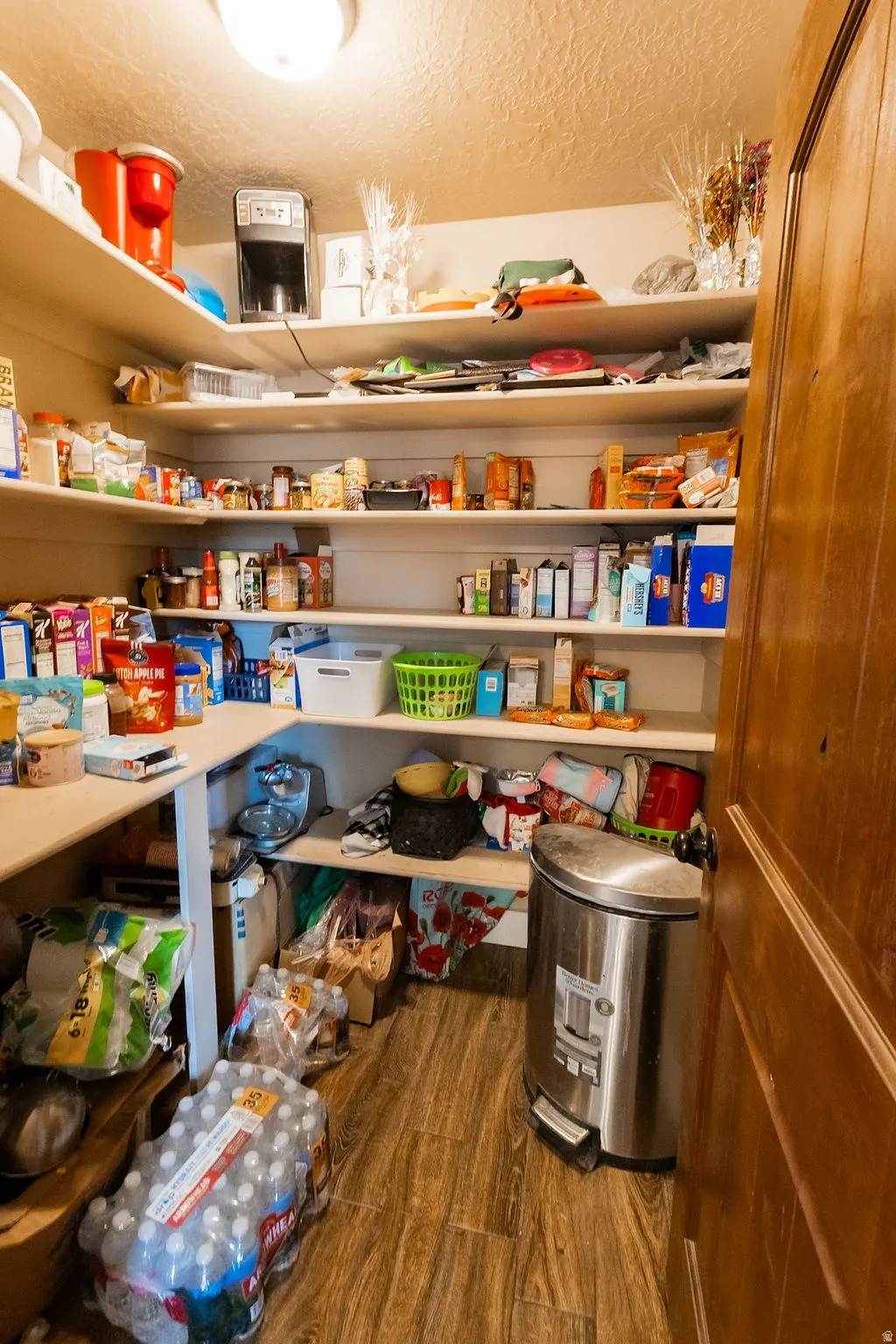 Walk-in pantry featuring extensive shelving, L-shaped countertop, wood-finish flooring, and a solid wood door