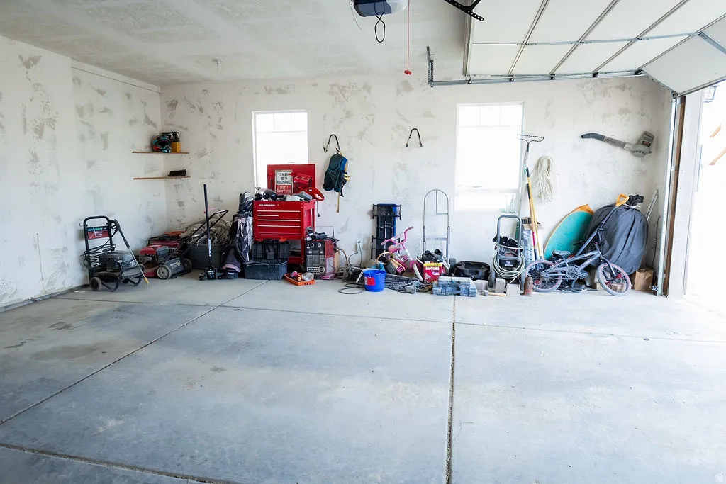 Concrete flooring garage with white walls, two windows, and an overhead garage door
