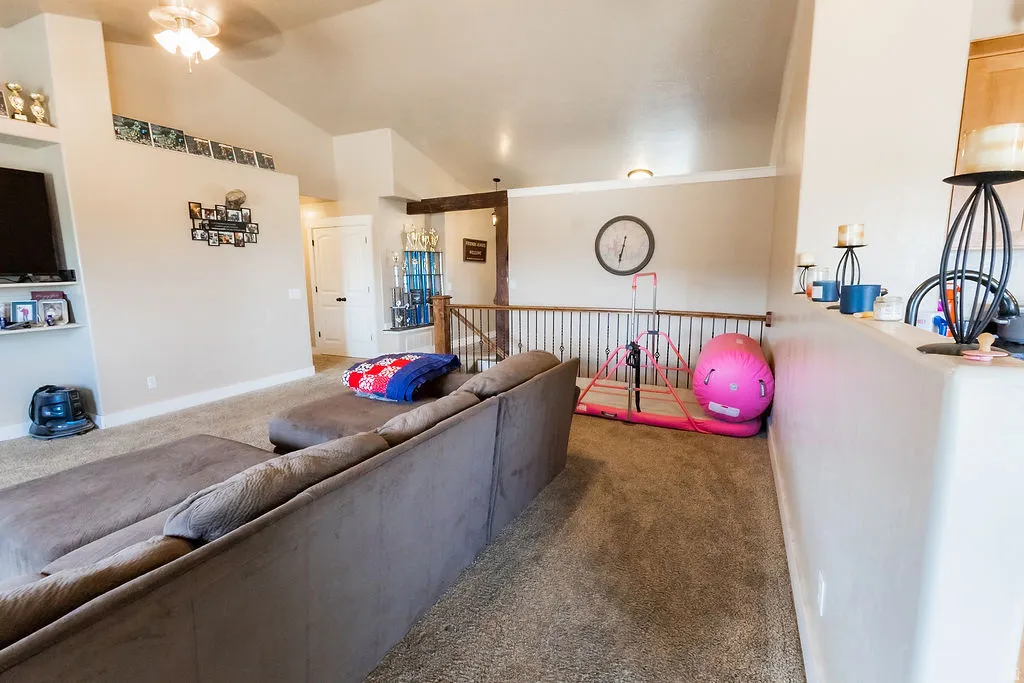 Carpeted living area featuring vaulted ceilings, a built-in media niche with shelving, and a ceiling fan