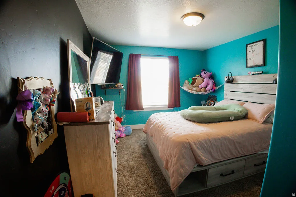 Carpeted room featuring a window with drapes, a light wood-finish bed frame with built-in storage drawers, and a ceiling-mounted light fixture