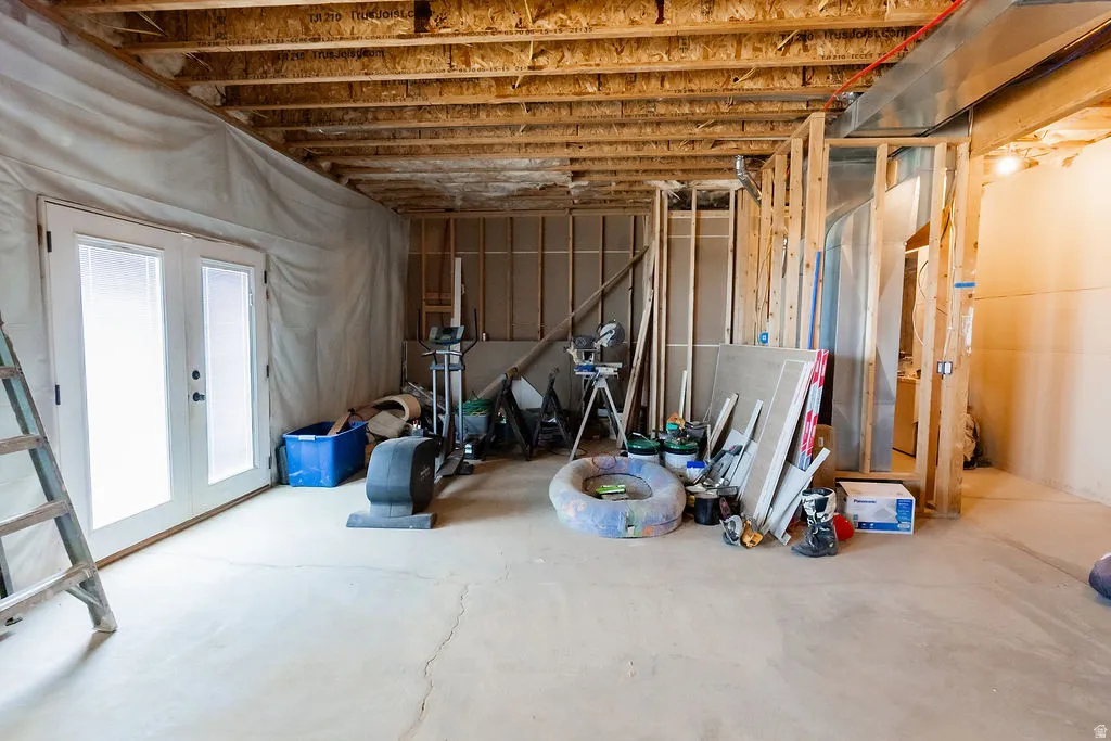Unfinished basement space featuring exposed ceiling joists, concrete flooring, and framing for future development