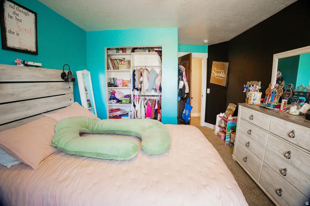 Bedroom featuring a built-in closet with shelving and hanging storage, wood-finish flooring, and a headboard with integrated sconce lighting