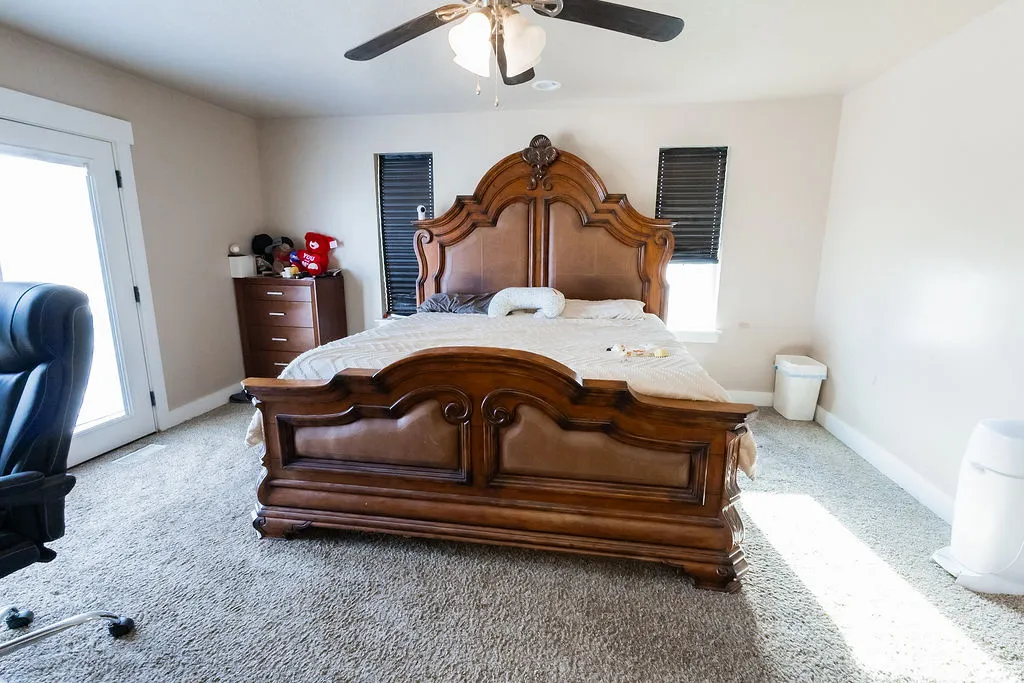 Light-colored carpeting throughout, featuring a ceiling fan with integrated lighting, and a white framed glass door
