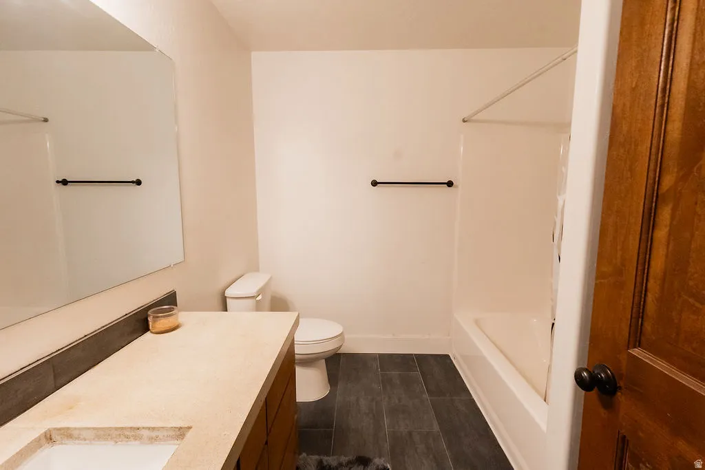Bathroom featuring a wood-finish vanity with an integrated sink and light-toned countertop, a large wall-mounted mirror, white toilet, and a white tub/shower combination