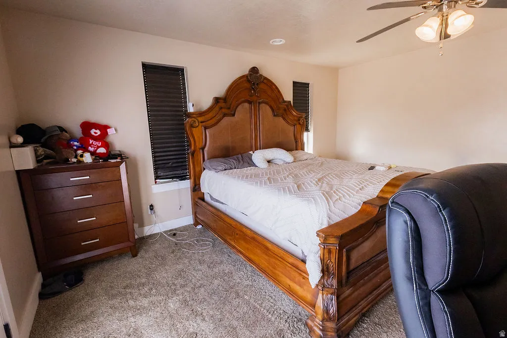 Carpeted room featuring neutral-toned walls, two windows with horizontal blinds, and a ceiling fan with integrated lighting