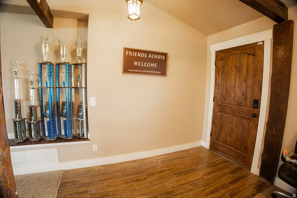 Arched wood-panel door with matte black hardware, wood-finish flooring, exposed ceiling beams, built-in display niche, and wall-mounted light fixture