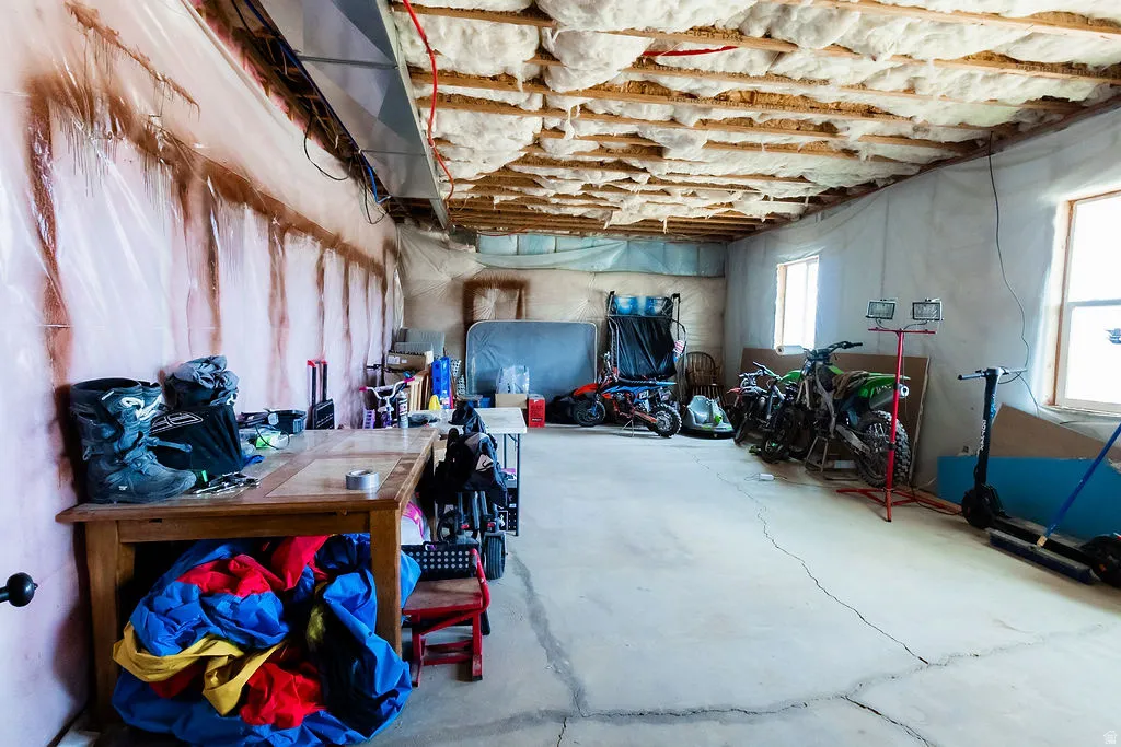 Unfinished basement with exposed ceiling joists and insulation, concrete flooring, and multiple windows providing natural light
