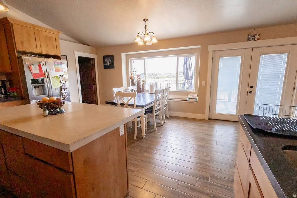 Kitchen and dining area featuring wood-finish flooring, light wood cabinetry, a central island with a light-toned countertop, a dining table with a built-in window bench, and French doors
