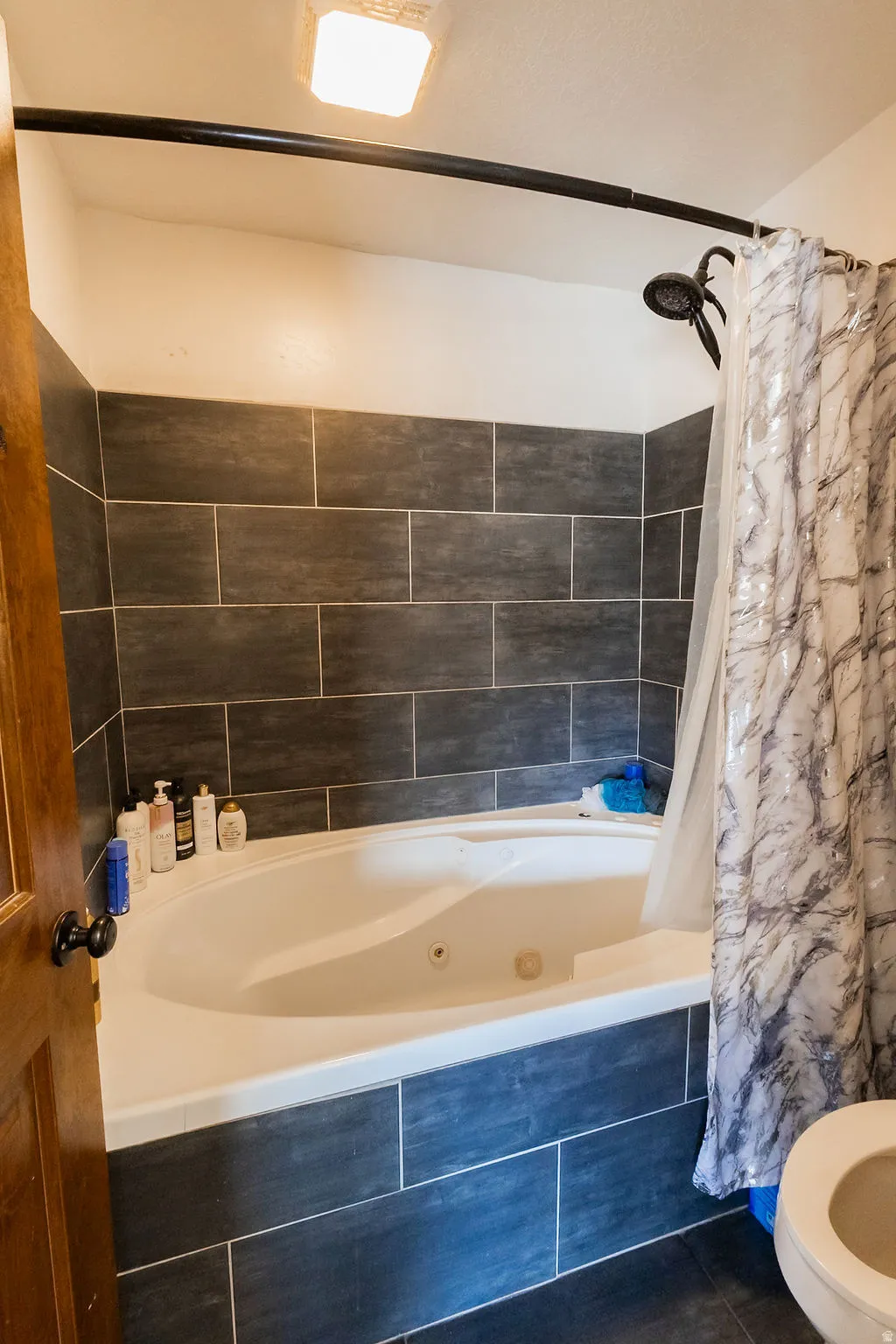 Bathroom featuring a jetted tub with dark rectangular tile surround and a coordinating dark tile floor