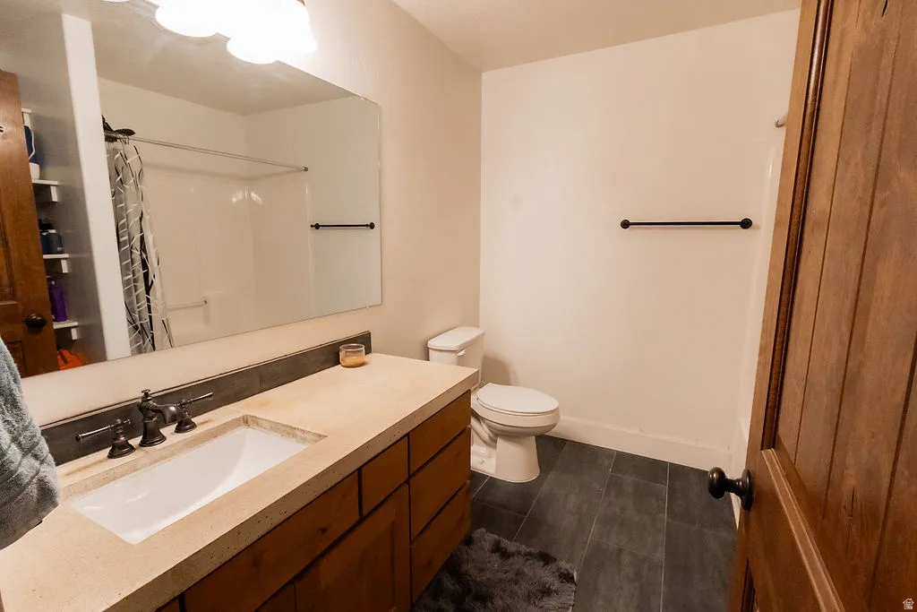 Bathroom featuring a wood-finish vanity with a built-in sink, a large wall-mounted mirror, and dark-toned tile flooring
