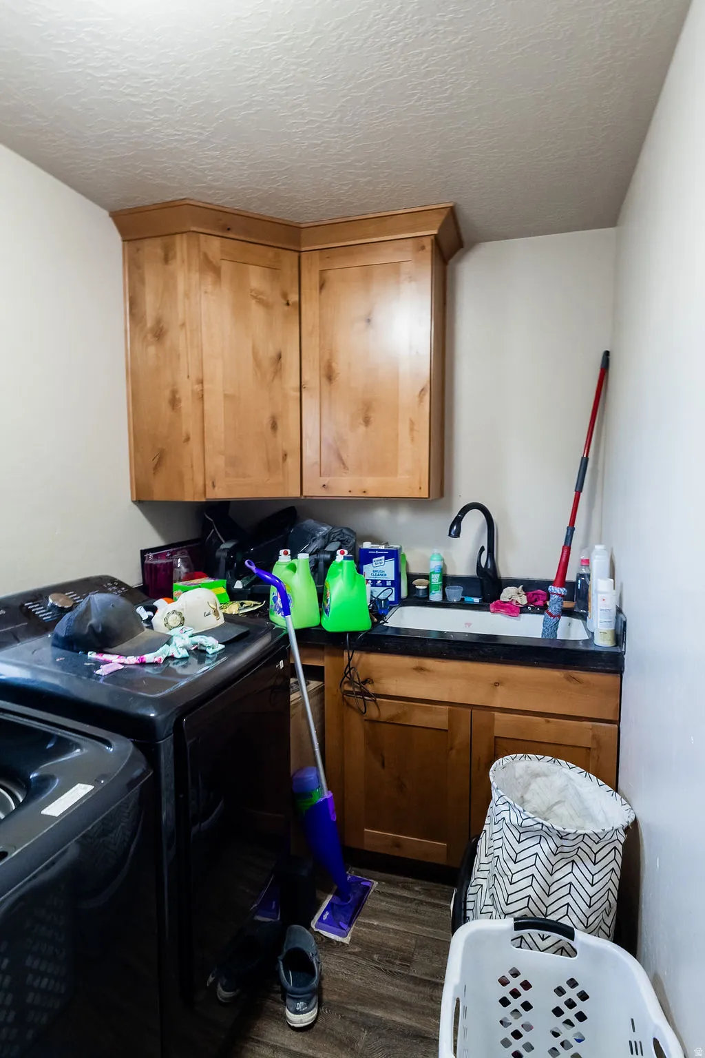 Laundry area featuring wood-finish cabinetry, a utility sink with a black faucet, and dark countertops