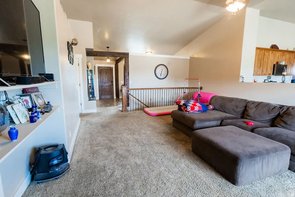 Carpeted loft area featuring a vaulted ceiling with a ceiling fan, a half wall with railing, and a built-in display shelf