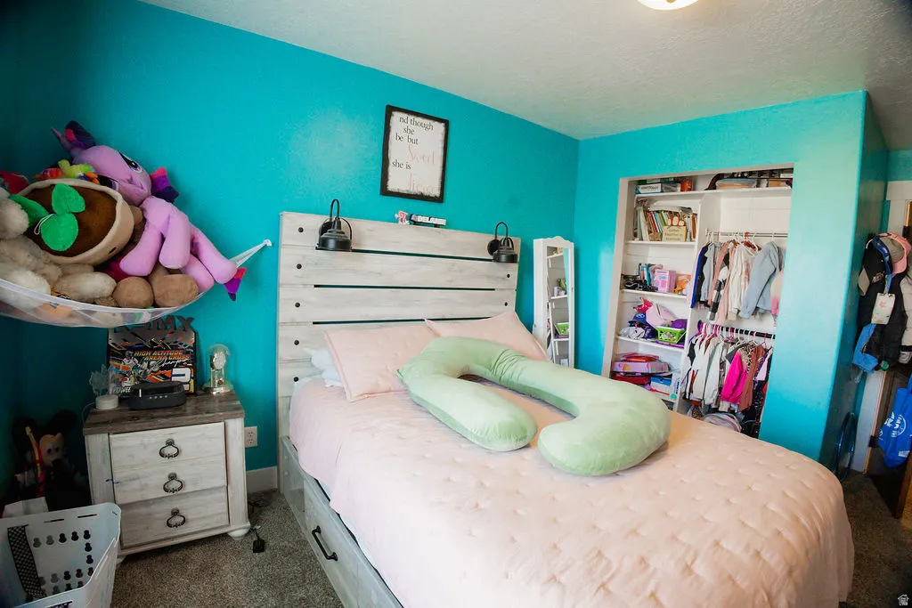 Bedroom featuring a light wood-finish headboard with integrated sconces, plush carpet flooring, and a recessed closet with shelving and hanging rods