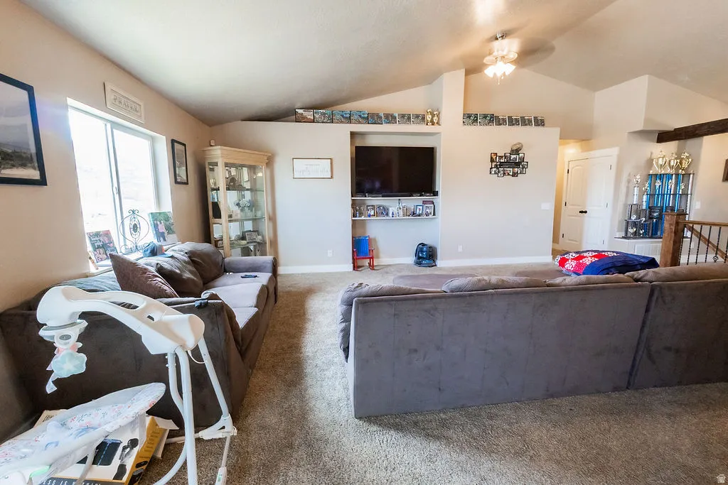 Spacious living area featuring vaulted ceilings, recessed wall niches, a ceiling fan, and carpeted flooring