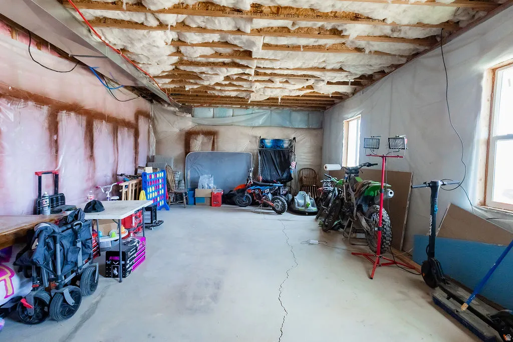 Unfinished basement space featuring exposed ceiling joists with insulation, concrete flooring, and multiple windows for natural light