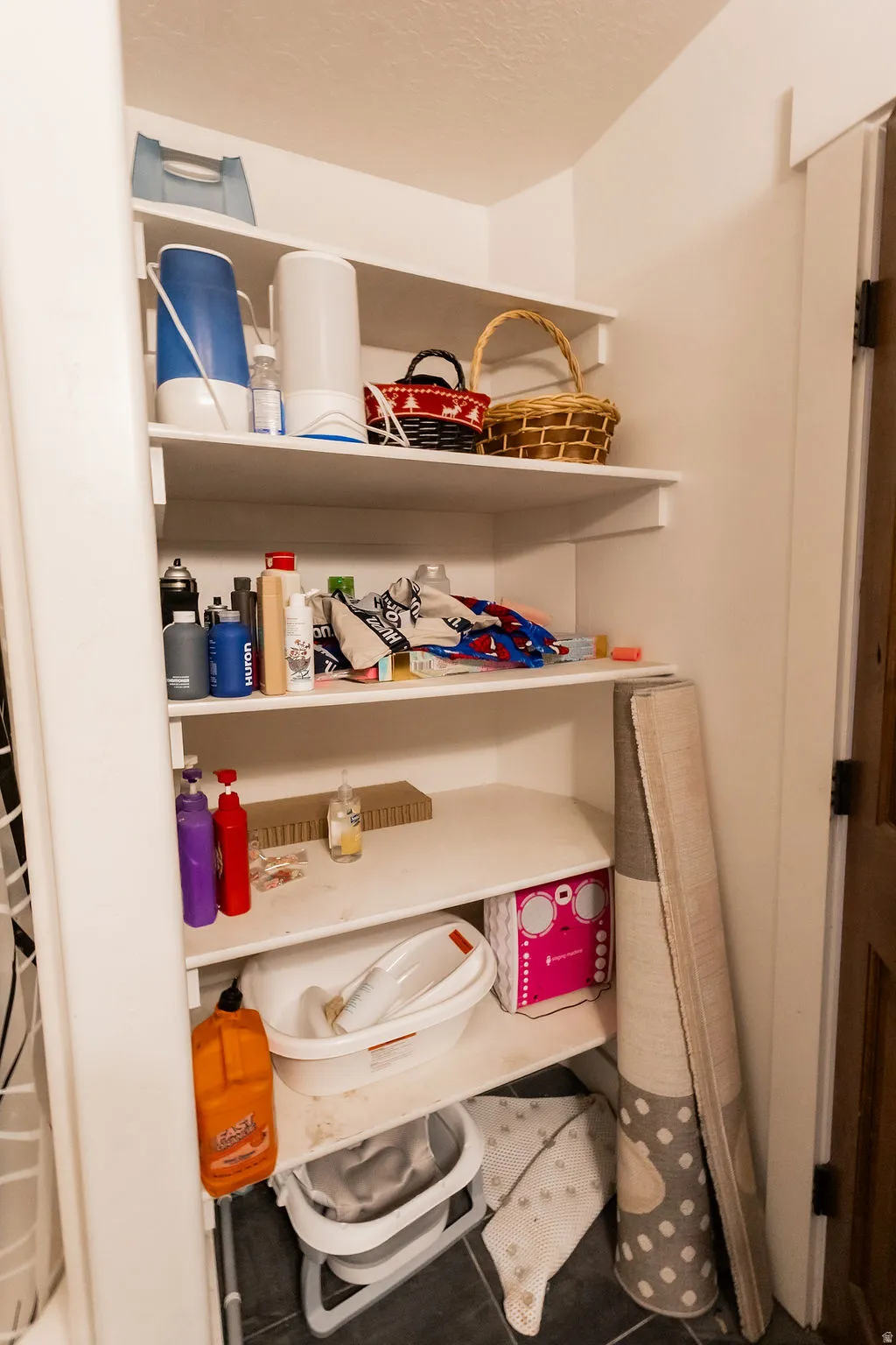 Built-in shelving for storage with white painted finishes, dark tile flooring, and a wood-finish door frame