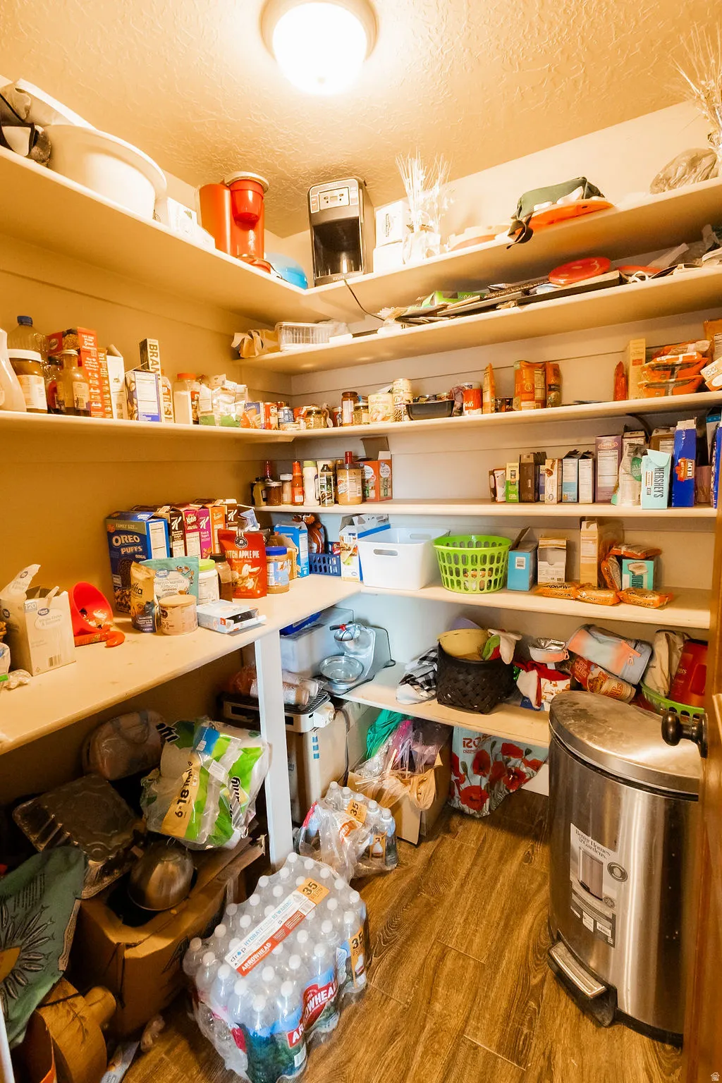 Walk-in pantry featuring extensive built-in shelving, wood-finish flooring, and overhead lighting