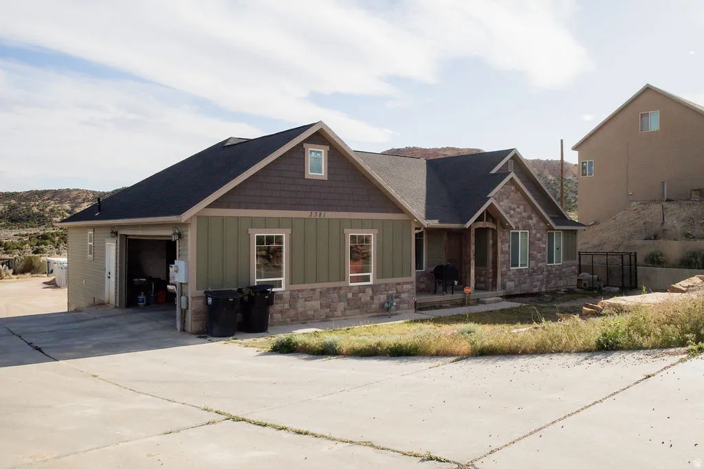 Ranch-style residence featuring a stone and siding exterior, an attached two-car garage, a covered front porch, a dark shingle roof, and multiple windows with white trim