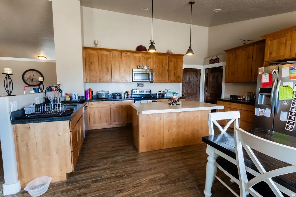 Kitchen featuring wood-finish flooring, light wood cabinetry, dark countertops, a central island with a light countertop, and stainless steel appliances