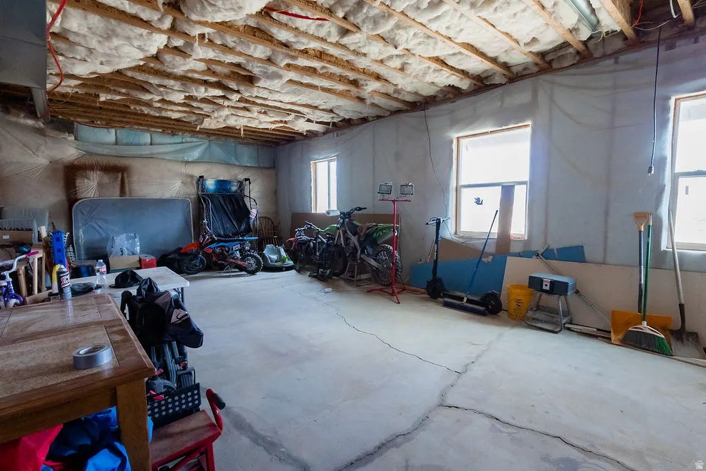 Unfinished basement featuring exposed ceiling joists with insulation, concrete flooring, and multiple windows providing natural light