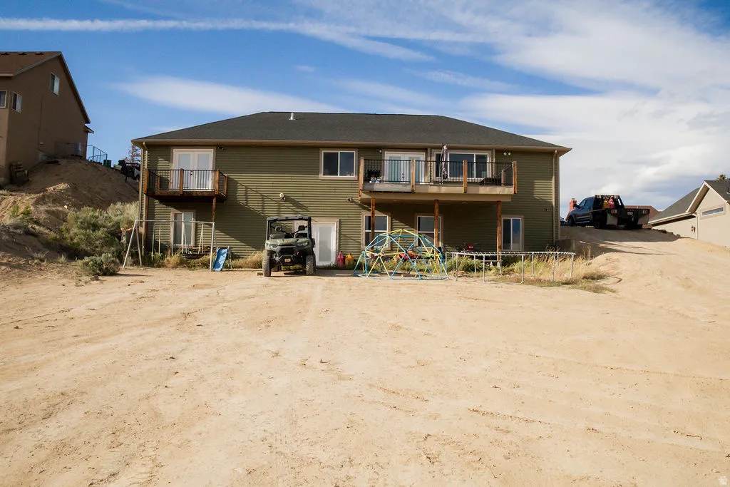 Rear exterior featuring two upper-level balconies with glass sliding doors, a lower-level patio with additional glass sliding doors, and a neutral-toned siding