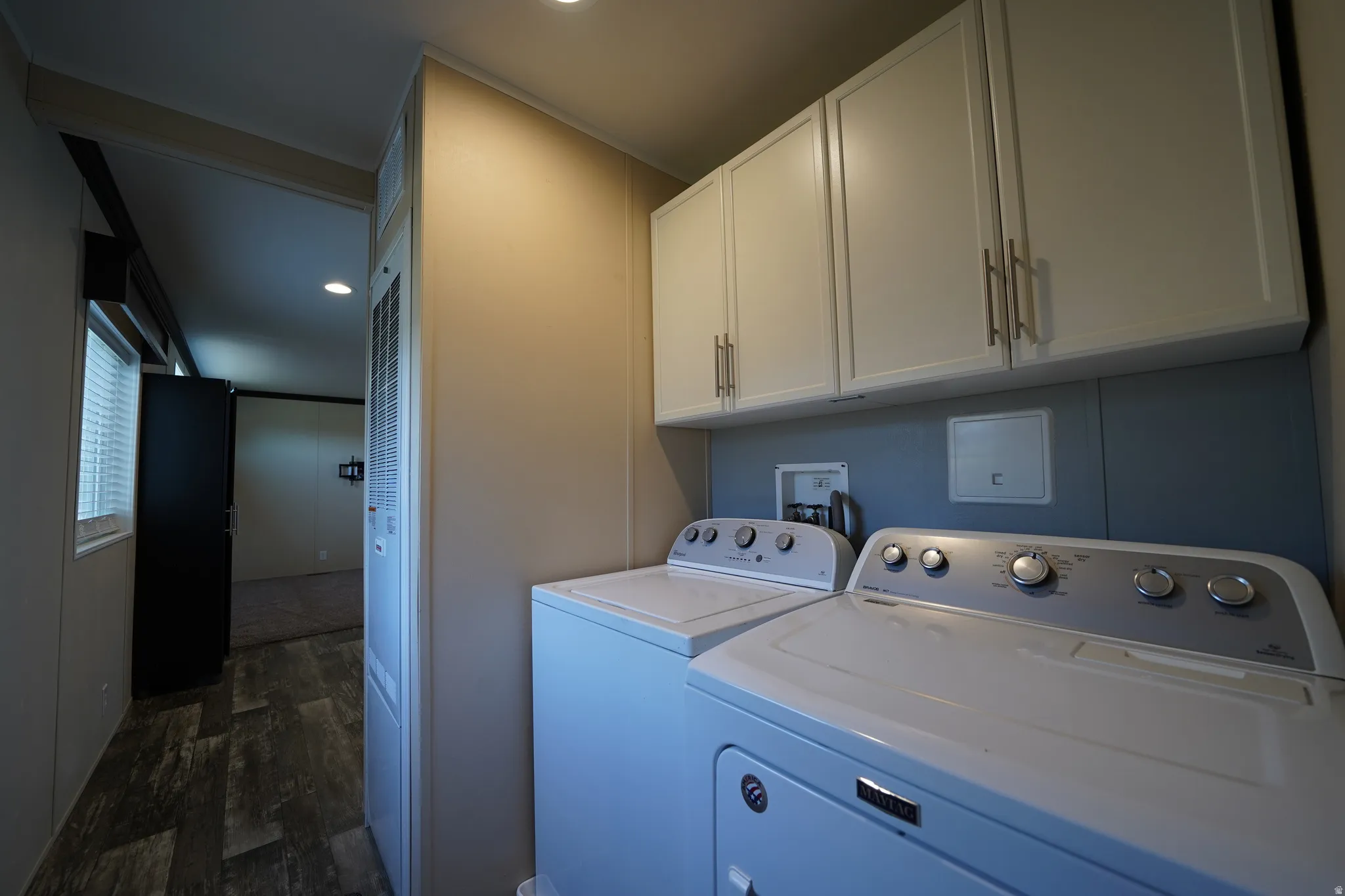 Dedicated laundry area featuring overhead white cabinetry with brushed nickel hardware, a blue accent wall, and wood-finish flooring