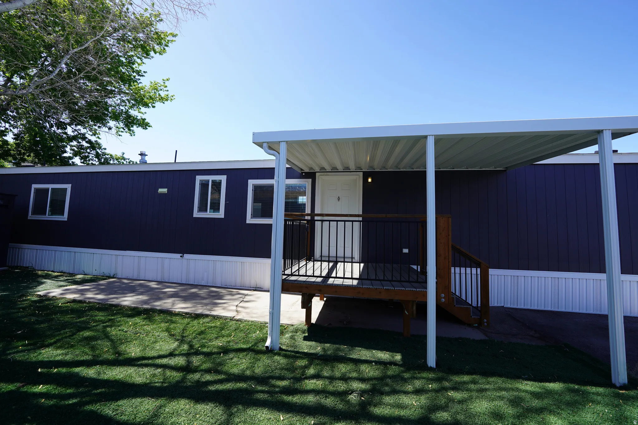 Exterior featuring dark blue siding, white trim, and a covered porch with dark wood steps and black railings