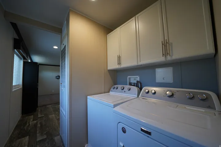 Dedicated laundry area featuring overhead white cabinetry with brushed nickel hardware, a blue accent wall, and wood-finish flooring