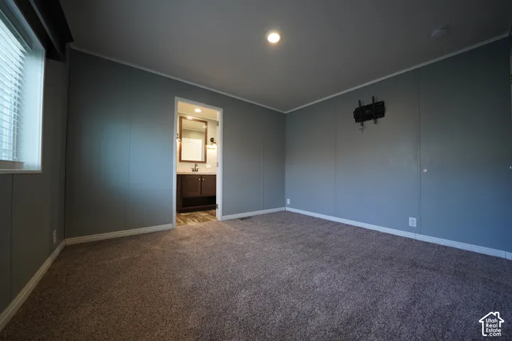Primary Bedroom - Carpeted interior space with a window featuring blinds, an overhead light fixture, and a doorway revealing a bathroom with a vanity, mirror, and sconce lighting