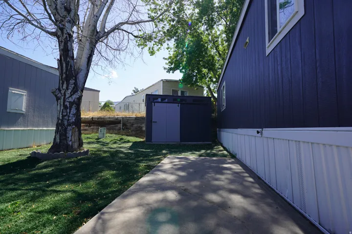 Paved walkway alongside the residence featuring dark vertical siding and white skirting