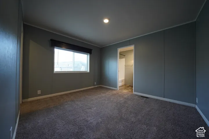 Primary Bedroom - Carpeted room featuring a window with blinds and a dark wood-finish valance, recessed ceiling lighting, and a doorway opening to a bathroom with a white bathtub and shower