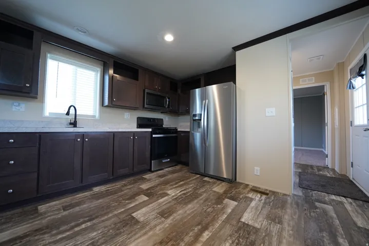 Modern kitchen featuring rich cabinetry, a stainless steel refrigerator, and wood-finish flooring