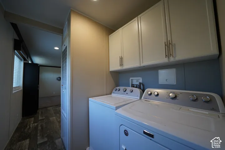 Dedicated laundry area featuring overhead white cabinetry with brushed nickel hardware, a blue accent wall, and wood-finish flooring