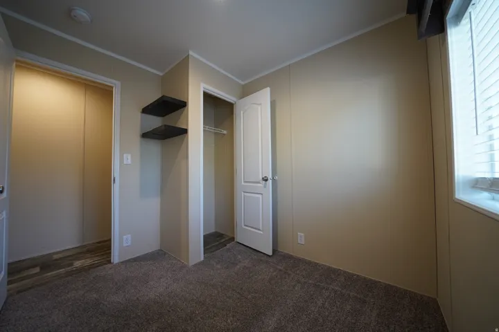 Bedroom 2 - Carpeted room featuring a window with horizontal blinds, built-in shelving, two open doorways, and ceiling trim