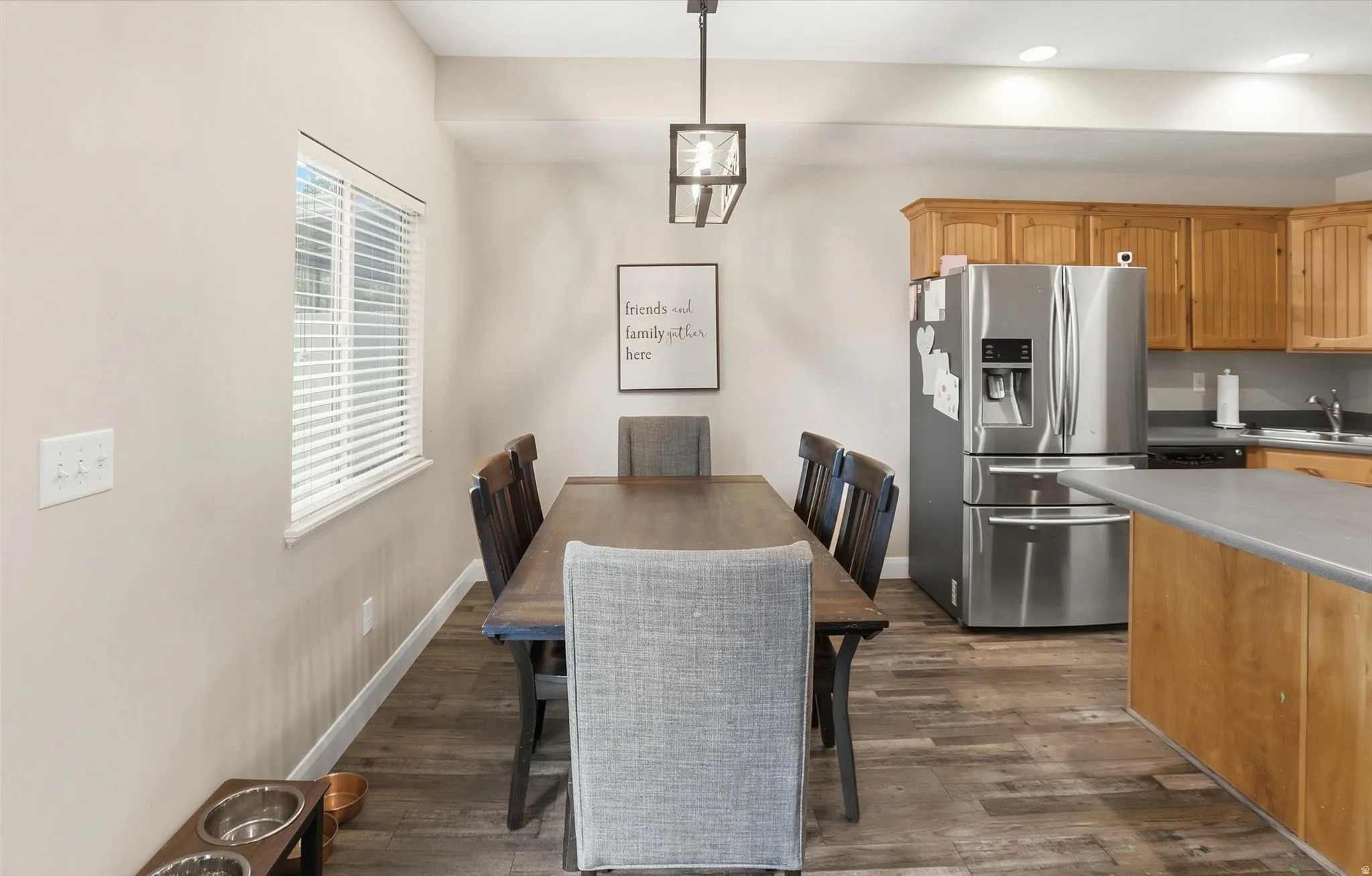 Open-concept dining area featuring wood-finish flooring, a contemporary linear chandelier, and a large window with blinds