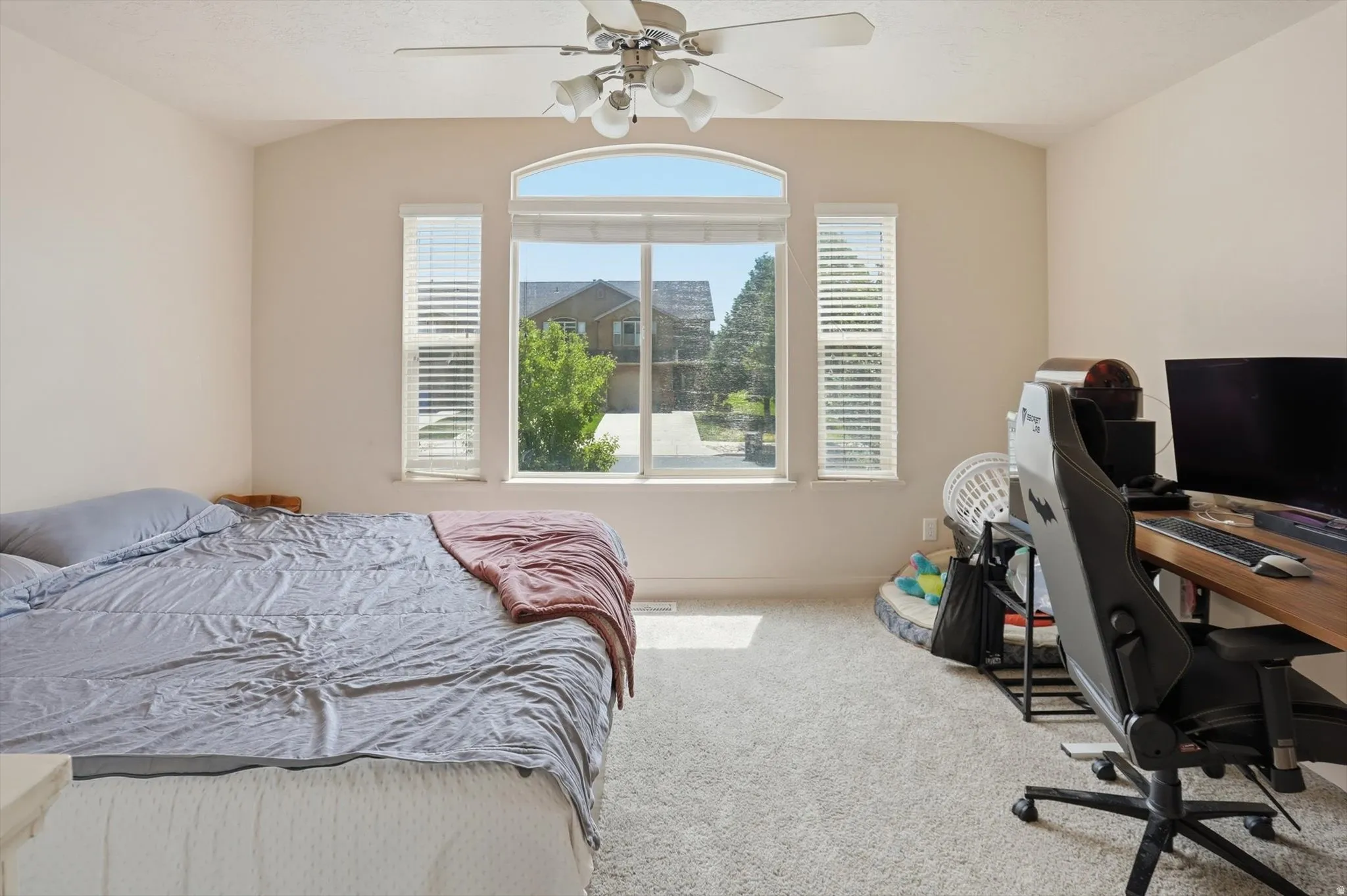 Carpeted room featuring a large arched window with side windows, a ceiling fan with light fixture, and vaulted ceilings