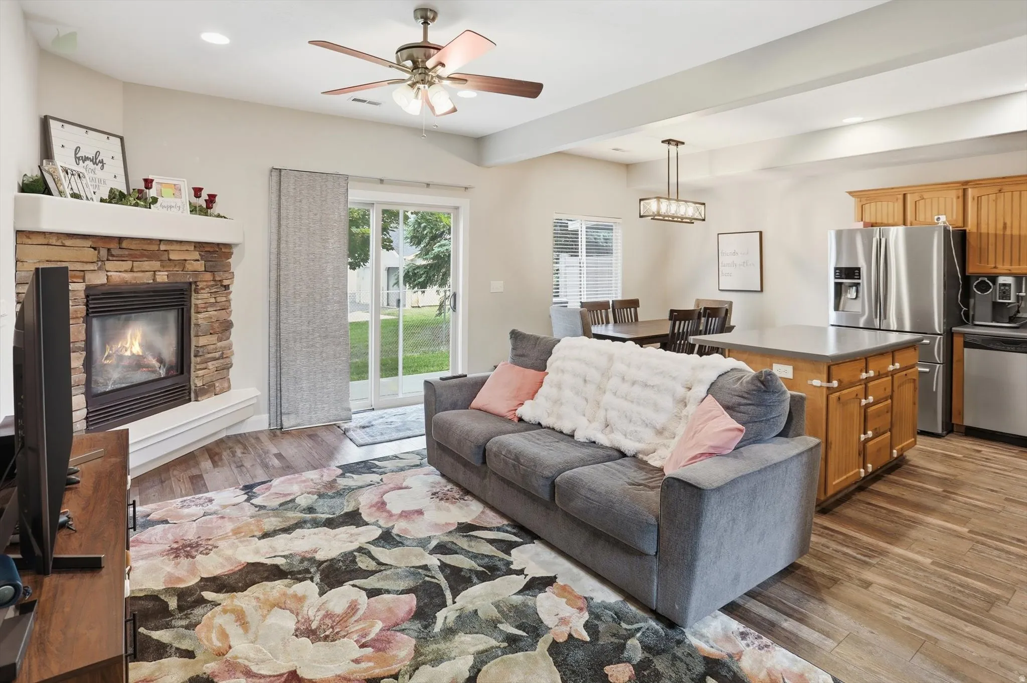 Open-concept living area featuring a stone-surround fireplace with mantel, sliding glass door to exterior, wood-finish flooring, a ceiling fan, and recessed lighting