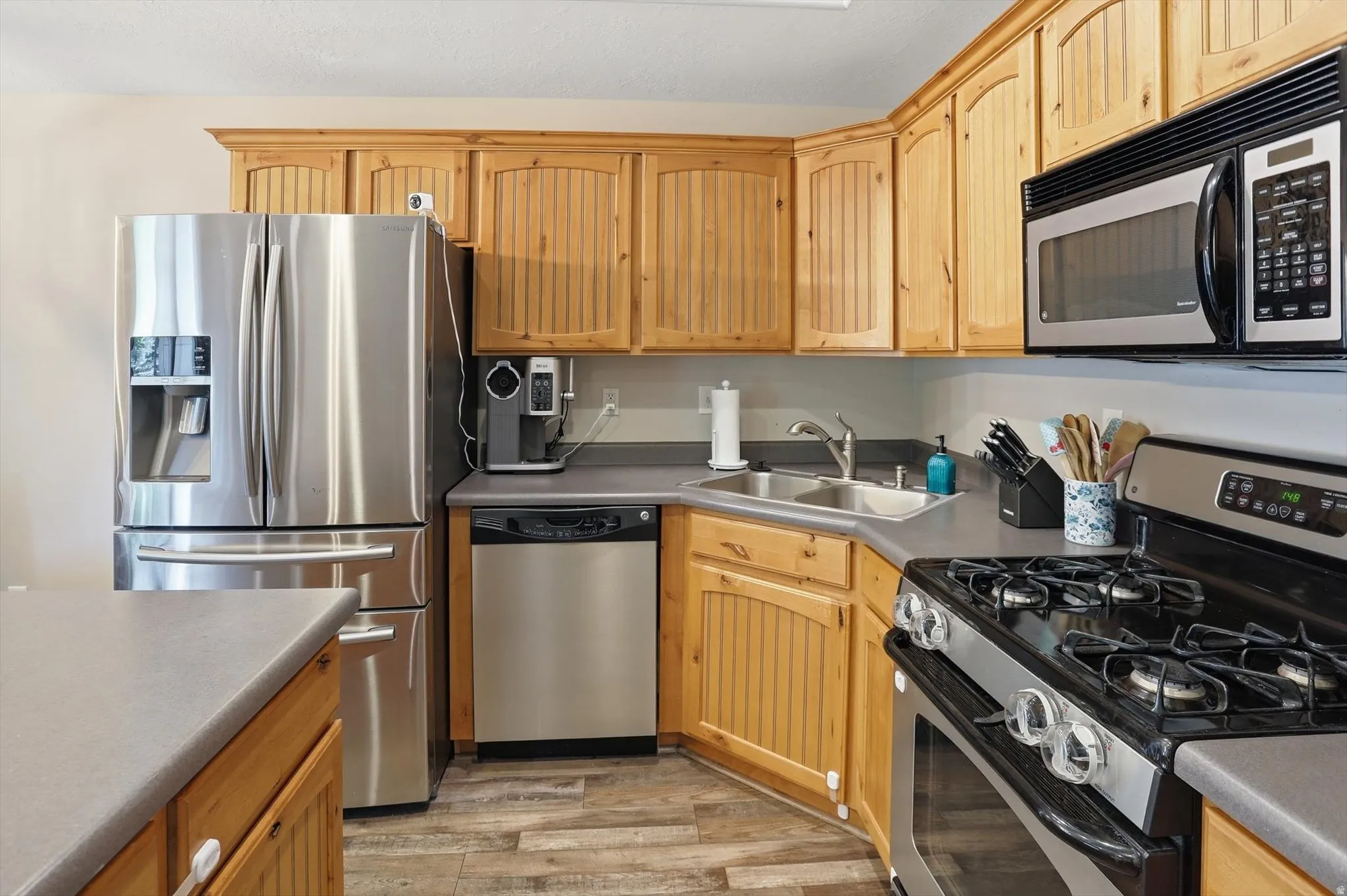 Kitchen featuring light wood cabinetry with beadboard accents, stainless steel appliances, a double-basin sink, and gray countertops