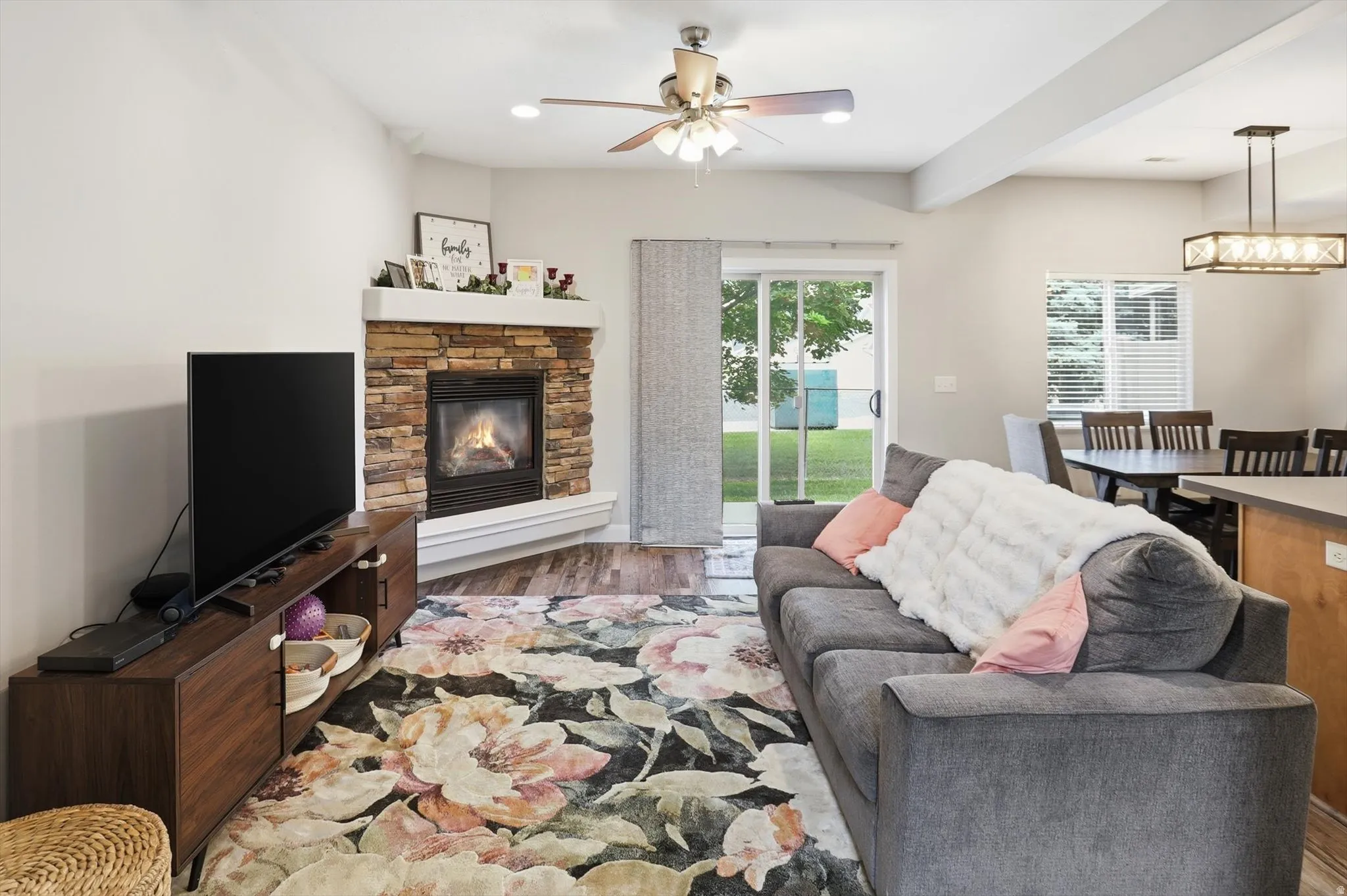 Cozy living space featuring a stone-clad corner fireplace with a white mantel, wood-finish flooring, and a ceiling fan