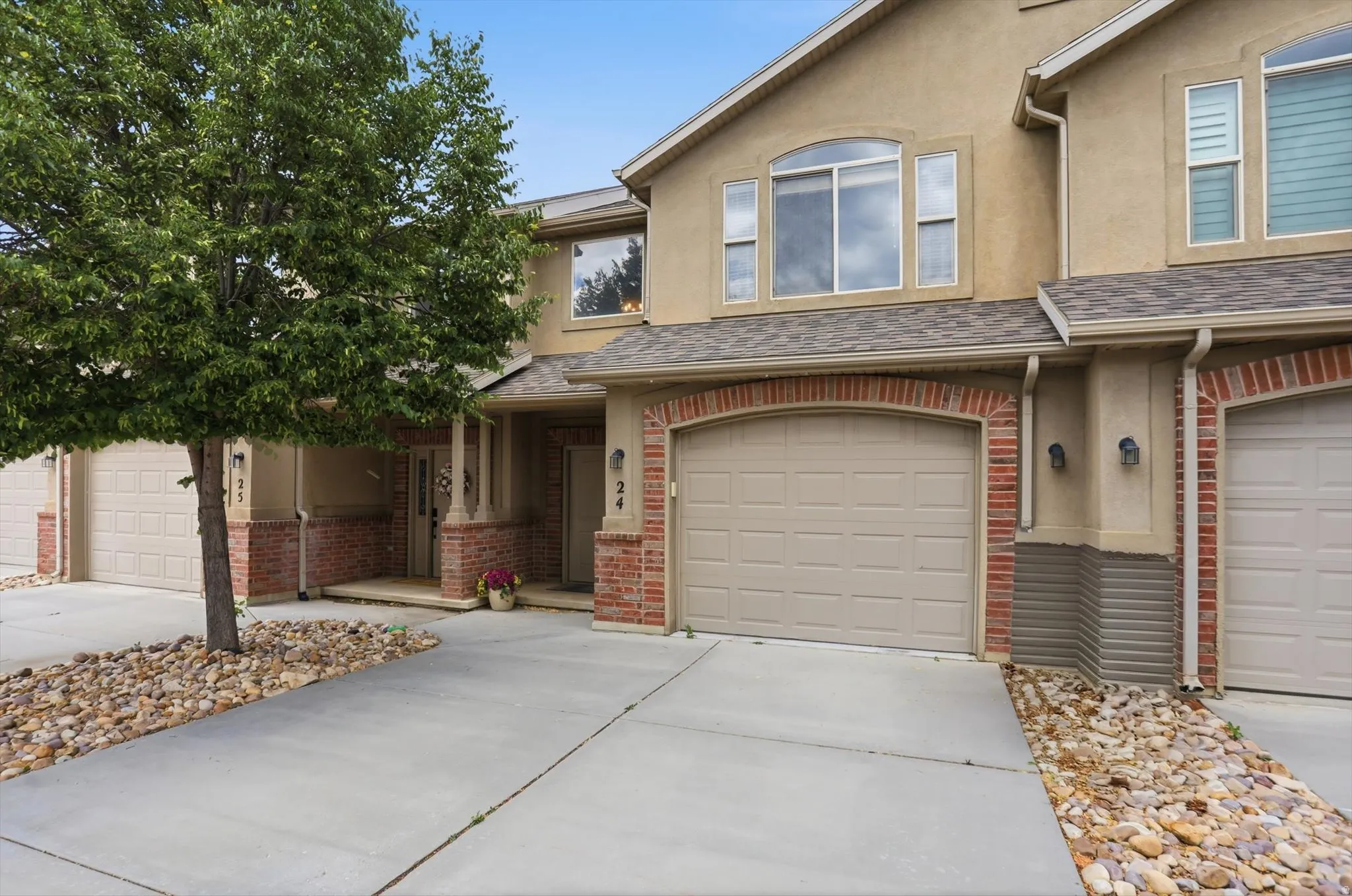 Exterior featuring tan stucco, brick veneer accents, and a shingle roof