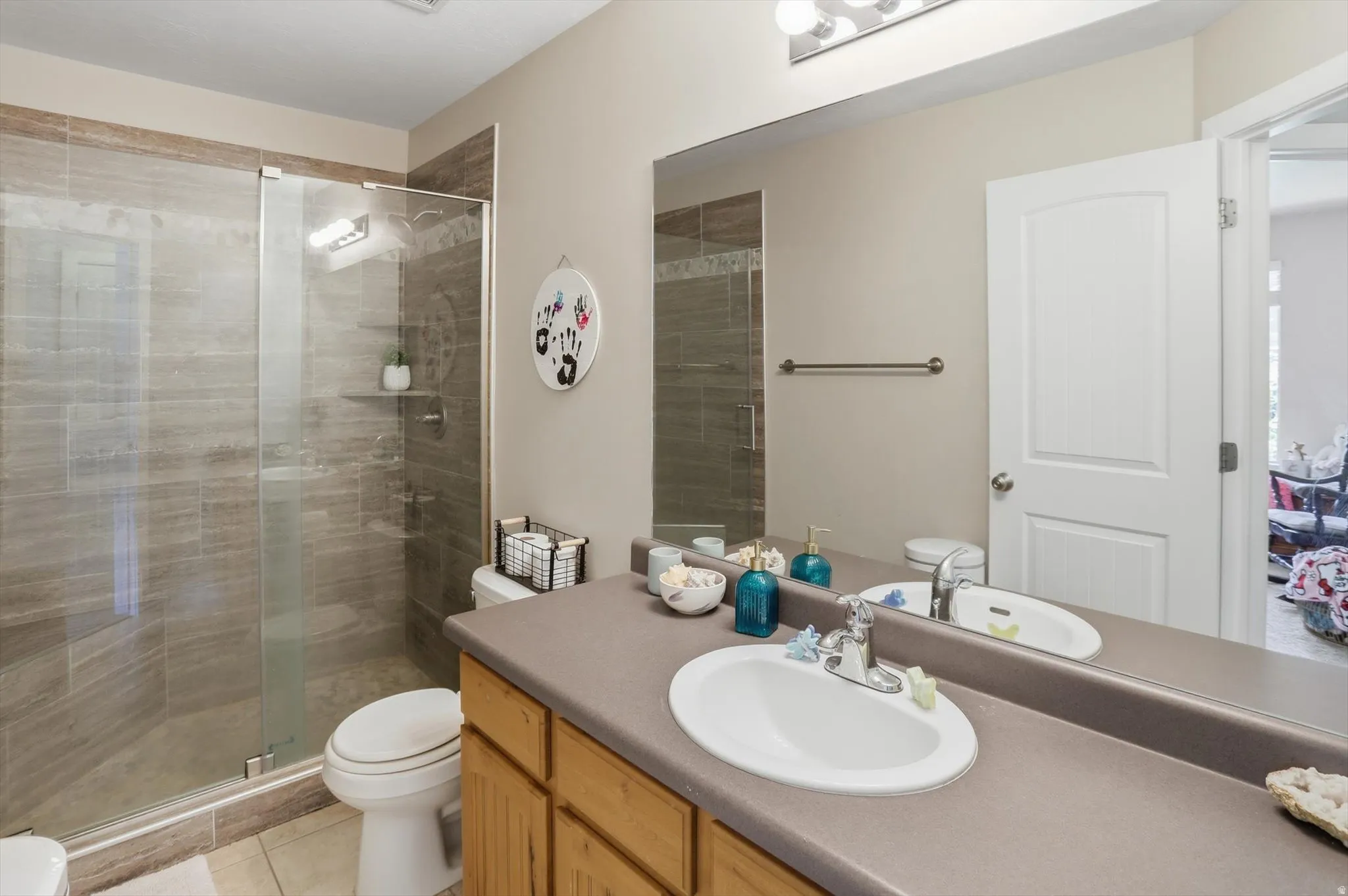 Bathroom featuring a glass-enclosed shower with tile surround, a single vanity with a laminate countertop, a large wall-mounted mirror, and wood-finish cabinetry