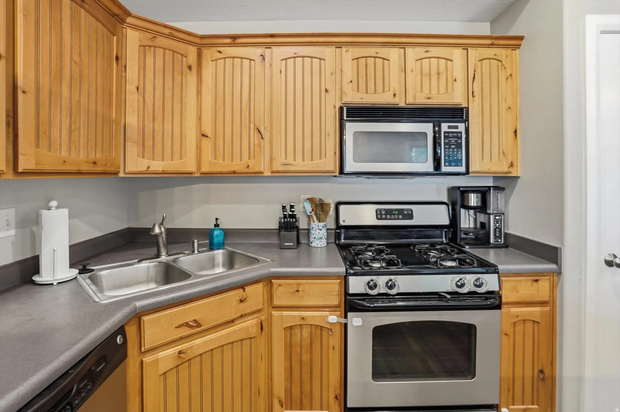 Kitchen featuring natural wood-finish cabinetry, stainless steel appliances, a double basin sink, and ample countertop space