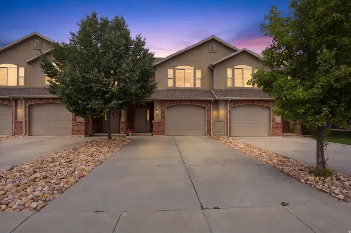 Multi-unit residence featuring arched garage doors with brick accents, concrete driveways, upper-level arched windows, and established trees
