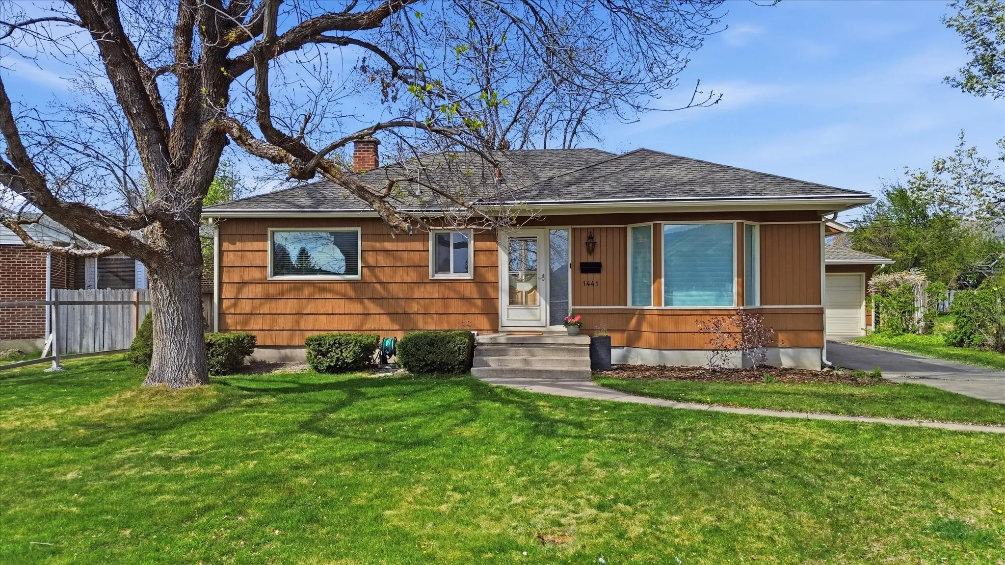 Ranch-style residence featuring a prominent bay window, a brick chimney, and a brown siding exterior