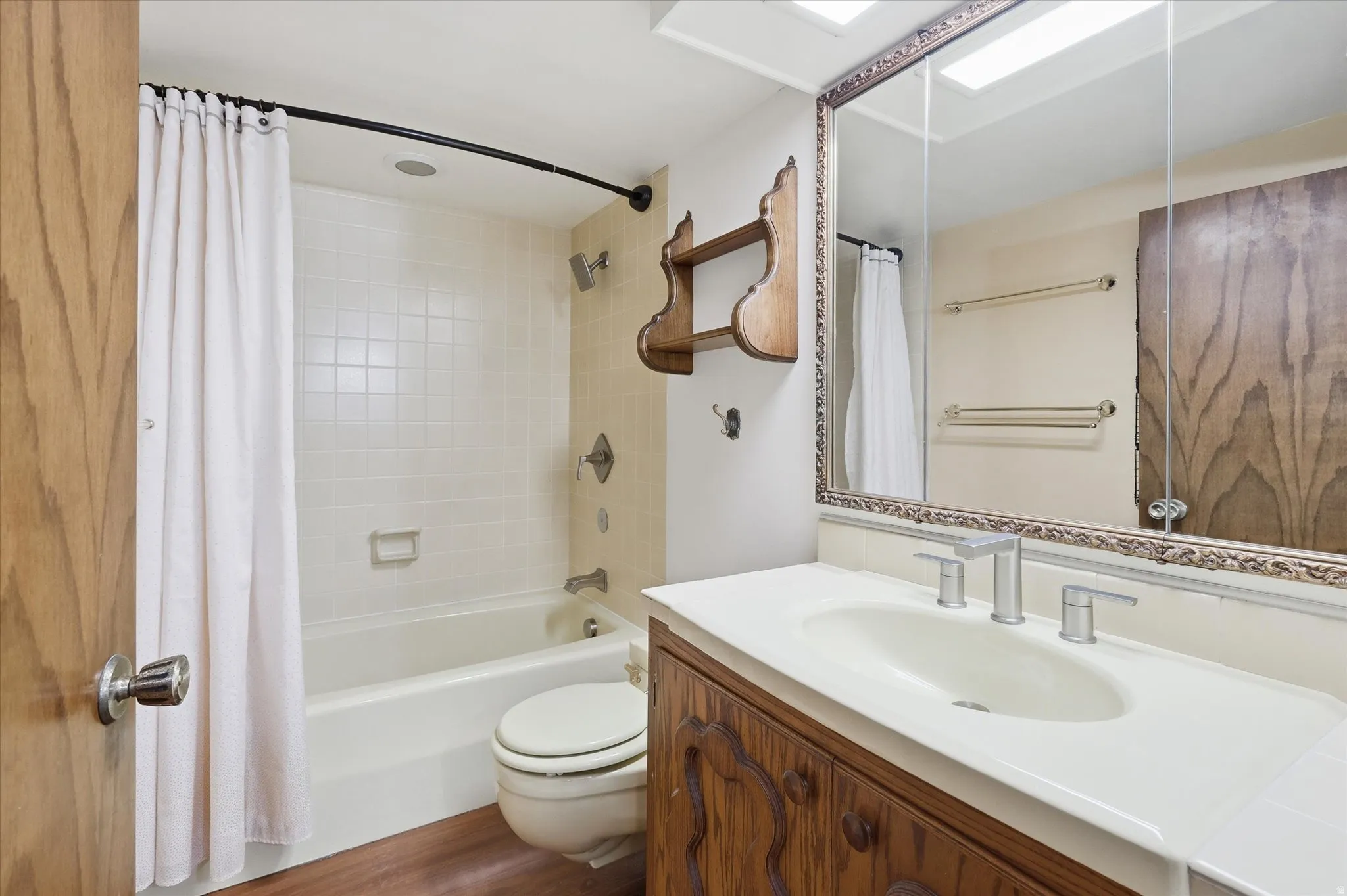 Full bathroom featuring a white tub with subway tile surround, a toilet, a vanity with a white countertop and oval sink, and a decorative framed mirror