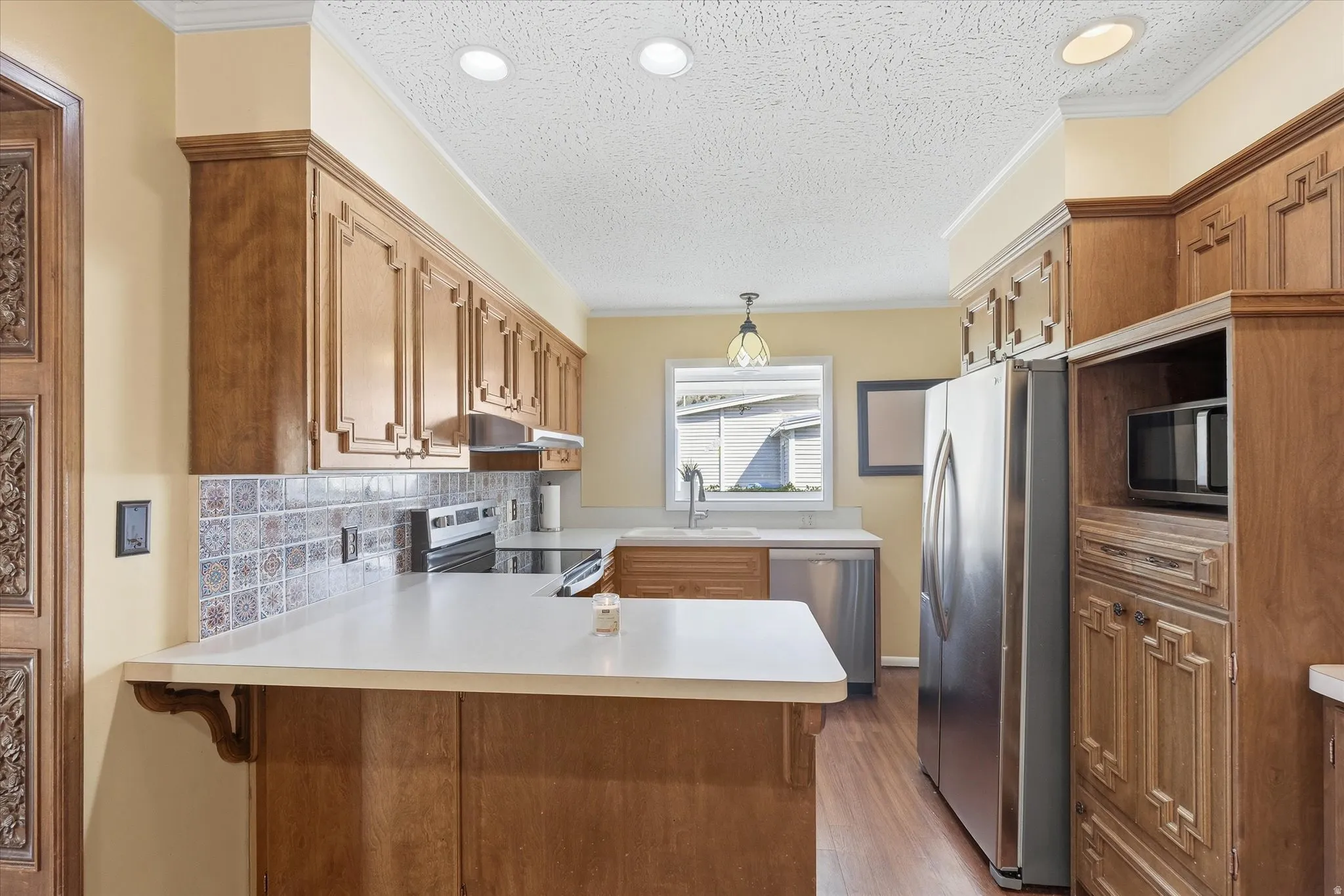 Kitchen featuring wood cabinetry, white countertops, a decorative tile backsplash, stainless steel appliances, and recessed lighting