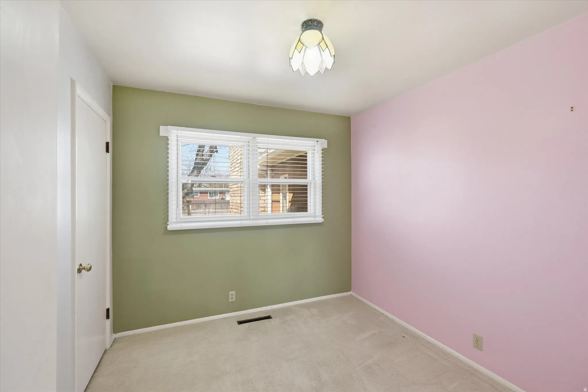 Interior room featuring a window with white blinds, neutral carpet, and a flush-mount ceiling light fixture